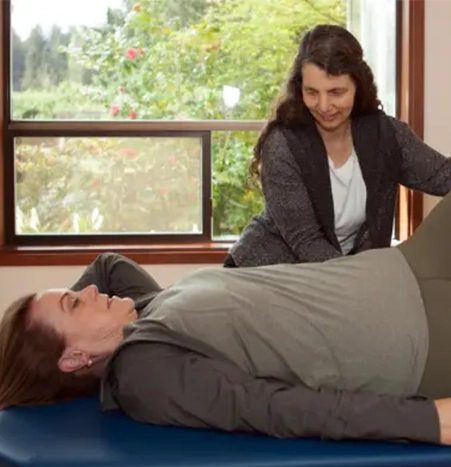 experience-the-benefits Laura using her hands to guide a fully clothed client lying on the table during a Feldenkrais lesson.