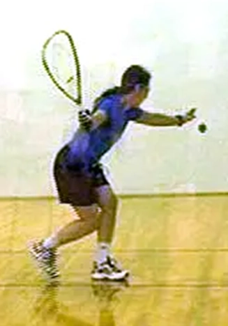 Laura Yedwab, a Kirkland Feldenkrais practitioner, serving the ball during a racquetball game on an indoor court.